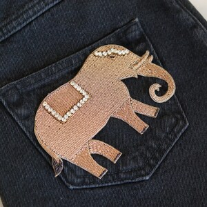 May include: A brown embroidered elephant patch with rhinestones on a black denim pocket.