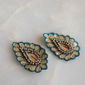 Puede incluir: Dos adornos decorativos azul turquesa y plata con un centro de cuentas. Los adornos tienen forma de lágrima y un acabado metálico plateado.