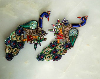 May include: Two embroidered peacock appliques. The peacocks feature blue, green, red, and gold thread with sequin embellishments. The appliques are detailed with intricate stitching and are designed with a vibrant color palette.