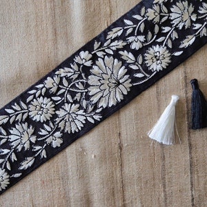 Pode incluir: Acabamento preto com bordado floral branco. O acabamento é mostrado com duas borlas, uma preta e uma branca.