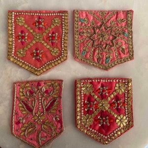 Puede incluir: Cuatro parches de tela rosa con bordados dorados y plateados. Los parches tienen forma de arco apuntado y presentan diseños florales y geométricos.