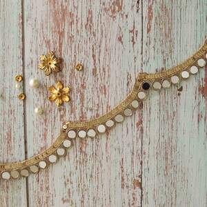 May include: Gold trim with round mirrored accents on a light blue wood background. There are also small gold and white embellishments scattered around the trim.