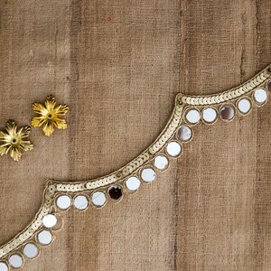May include: A gold trim with round mirror embellishments on a brown fabric background. Two gold star-shaped embellishments are also visible.