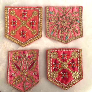 Puede incluir: Cuatro parches de tela cuadrados con bordes inferiores puntiagudos sobre fondos de color rosa coral. Cada parche está decorado con intrincados bordados metálicos dorados, pequeñas cuentas blancas y detalles de hilo rosa y naranja en motivos florales.