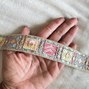 May include: A beige, embroidered trim with colorful floral and geometric patterns. The trim is made of a sheer fabric and has a delicate, feminine look.