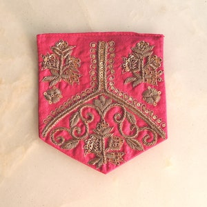 Puede incluir: Una bolsa de tela rosa con bordados dorados con diseños florales y paisley. La bolsa está decorada con lentejuelas.