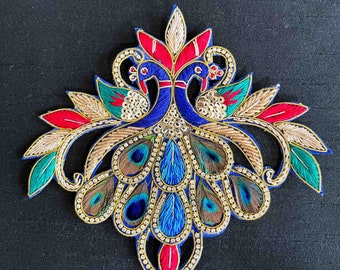 May include: A blue and gold embroidered peacock design with red, green, and white accents. The peacock has a spread tail with blue, green, and gold feathers. The design is embellished with rhinestones.