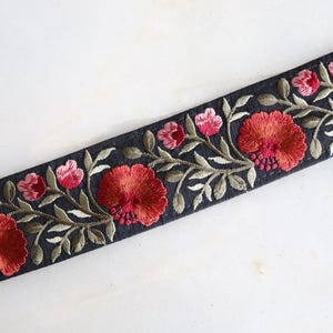 Pode incluir: Acabamento de tecido preto com flores vermelhas e rosa e folhas verdes bordadas.