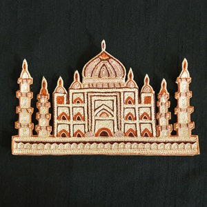 Op de afbeelding: Een gedetailleerd geborduurd ontwerp van een moskee, met ingewikkelde details in witte en bruine draad op een zwarte achtergrond.