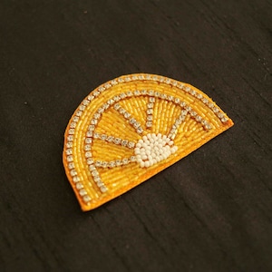 Puede incluir: Una aplicación de cuentas amarillas y blancas en forma de semicírculo. La aplicación está decorada con pequeñas cuentas blancas y diamantes de imitación plateados.