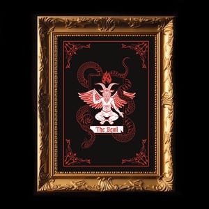 May include: A framed illustration of the Devil card from a tarot deck. The card features a red and white illustration of a horned figure with wings, surrounded by a red snake. The text "The Devil" is written in red at the bottom of the card.