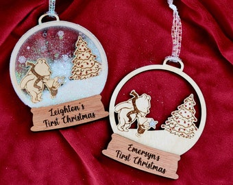 Può includere: Due decorazioni natalizie in legno. Una è una palla di neve con glitter e un orso che tiene una stella, il testo "Leighton's First Christmas". L'altra è un ornamento in legno con un orso e un albero, il testo "Emersyn's First Christmas".