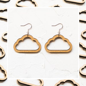 Op de afbeelding: Een paar houten oorbellen in de vorm van een wolk met zilveren haakjes. De oorbellen zijn lichtbruin en hebben een eenvoudig, minimalistisch ontwerp.