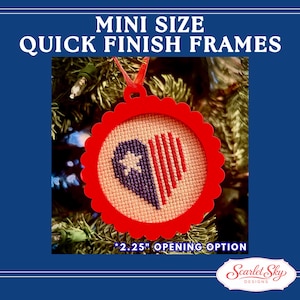 Op de afbeelding: Een rode, geschulpte ornament met een kruissteekontwerp van een hart en ster in blauw en rood. De tekst "MINI SIZE QUICK FINISH FRAMES" en "2.25" OPENING OPTION" zijn zichtbaar. De ornament hangt aan een kerstboom.