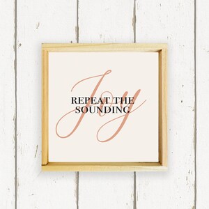 May include: A framed print with a peach-colored cursive word "Joy" and the text "Repeat the Sounding" in black.