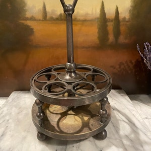 May include: A silver-toned metal egg holder with a handle. The holder has two tiers, each with six circular indentations for eggs. The holder is on a white marble surface.