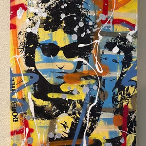 May include: Abstract portrait art on canvas featuring a figure wearing sunglasses, with black curly hair, and the name "BOB" visible. The background is a mix of yellow, blue, orange, and white paint splatters and brushstrokes, creating a vibrant and energetic composition.