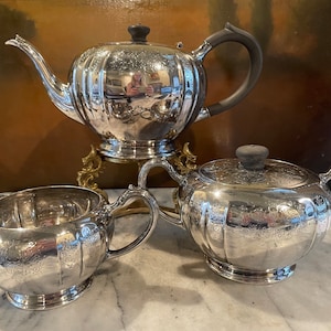 May include: A silver tea set with a teapot, creamer, and sugar bowl. The set has an ornate design and is in excellent condition.