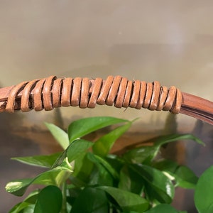 Puede incluir: Primer plano de un asa de mimbre marr&oacute;n tejido en una cesta redonda.