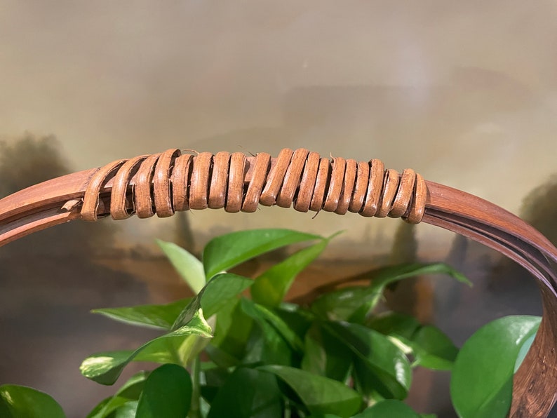 Puede incluir: Primer plano de un asa de mimbre marr&oacute;n tejido en una cesta redonda.