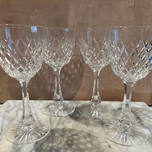 May include: Four clear crystal wine glasses with diamond-cut patterns. The glasses have long stems and round bases. The glasses are arranged on a marble surface.