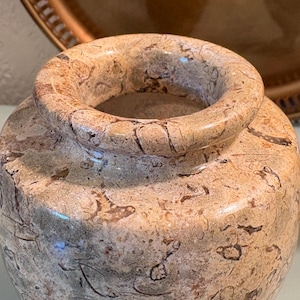 Puede incluir: Un jarr&oacute;n peque&ntilde;o y redondo con una abertura ancha. El jarr&oacute;n est&aacute; hecho de un material similar a la piedra con un patr&oacute;n moteado de beige, marr&oacute;n y gris. La superficie tiene un acabado pulido y la forma general es simple y elegante.
