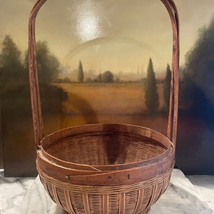 Puede incluir: Una cesta grande, redonda y tejida con un acabado marr&oacute;n natural. La cesta tiene un solo asa arqueada hecha del mismo material tejido.