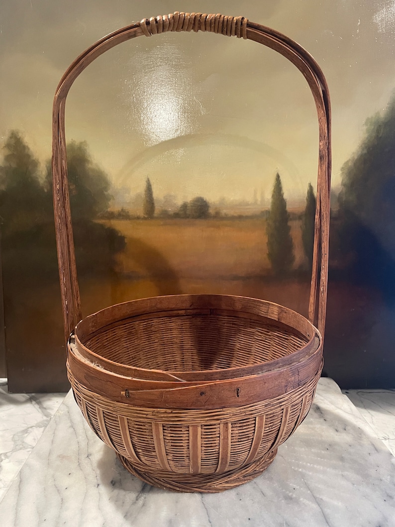 Puede incluir: Una cesta grande, redonda y tejida con un acabado marr&oacute;n natural. La cesta tiene un solo asa arqueada hecha del mismo material tejido.