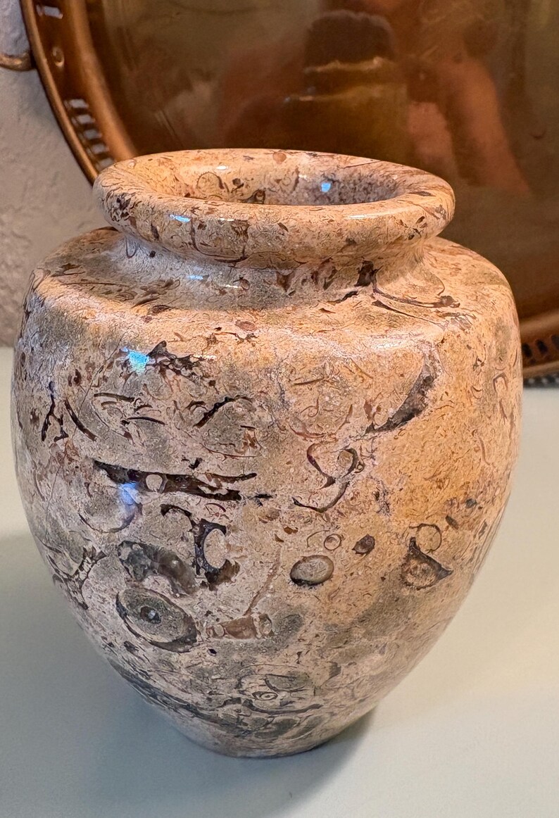 Puede incluir: Un jarr&oacute;n decorativo moteado, con un cuerpo redondeado y una peque&ntilde;a abertura acampanada. El jarr&oacute;n tiene una combinaci&oacute;n de colores beige y marr&oacute;n con patrones intrincados. El recipiente probablemente est&eacute; hecho de piedra o un material similar.