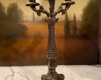 May include: A three-armed, ornate, gold-toned metal candelabra with a decorative base and three candle holders.