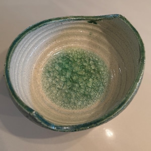 May include: A green and white ceramic bowl with a speckled glaze. The bowl has a rounded shape and a slightly uneven rim.
