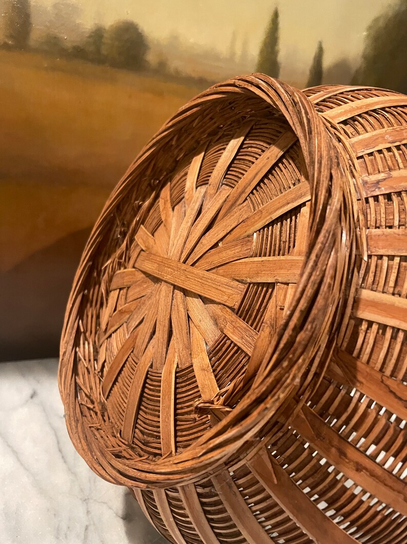 Puede incluir: Una cesta de mimbre marr&oacute;n con una parte superior redonda y abierta y un patr&oacute;n tejido. La cesta est&aacute; hecha de materiales naturales y tiene un aspecto r&uacute;stico.