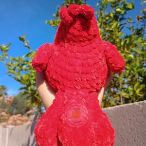 May include: A bright red plush bird toy crafted from soft, textured yarn. The bird features a rounded body, small wings, and a prominent tail. A circular logo with the text Playful Creations is visible on the lower section of the tail feathers.