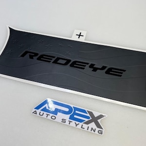 Puede incluir: Una calcomanía para coche negra y plateada con la palabra "REDEYE" en letras negras. El diseño presenta un patrón ondulado y estrellas. También se ve el logotipo de Apex Auto Styling.