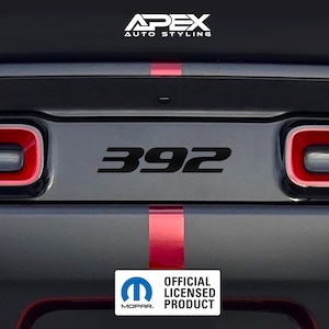 Può includere: Emblema nero "392" sul pannello posteriore di un'auto, con accenti rossi e grigi. L'immagine include il logo "Apex Auto Styling" e il logo Mopar "Official Licensed Product".
