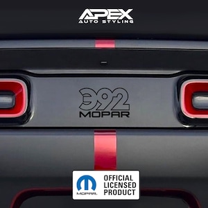 Può includere: Primo piano della parte posteriore di un'auto con dettagli neri e rossi. L'immagine presenta il testo "392 MOPAR" in nero, insieme al logo "OFFICIAL LICENSED PRODUCT". Il design dell'auto include strisce rosse.