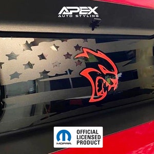 May include: Black car panel with a cut-out American flag design and a red and orange Hellcat logo. The text "APEX AUTO STYLING" is at the top. The bottom right corner has the Mopar official licensed product logo.