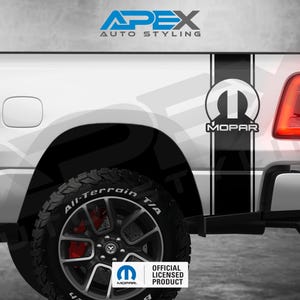 Könnte beinhalten: Weißes LKW-Heck mit schwarzen Rennstreifen und einem Mopar-Logo. Der LKW hat schwarze Reifen mit roten Bremssätteln und dem Text "All-Terrain T/A". Der Text "APEX AUTO STYLING" befindet sich oben.