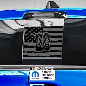 May include: A black and gray graphic of the American flag with a ram head design. The image is on a vehicle's rear window. The bottom right corner has a white sticker with the text "Customizable" and "Official Licensed Product".