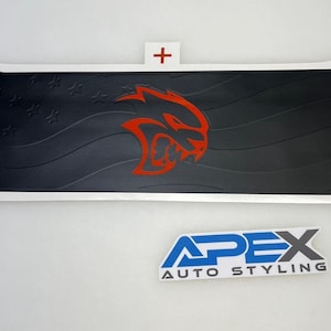 Puede incluir: Gráfico en blanco y negro con un logotipo rojo de Hellcat y un diseño de bandera estadounidense. El gráfico tiene forma de bandera con un borde blanco. El texto "APEX AUTO STYLING" está debajo.