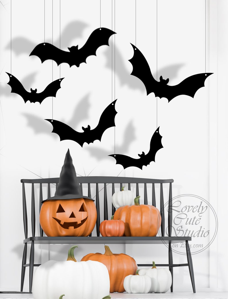 May include: A black wooden bench with a carved back and a pumpkin with a witch's hat on top. The pumpkin is carved with a jack-o'-lantern face. There are several pumpkins of different sizes and colors on the bench. There are also black bats hanging from the ceiling.