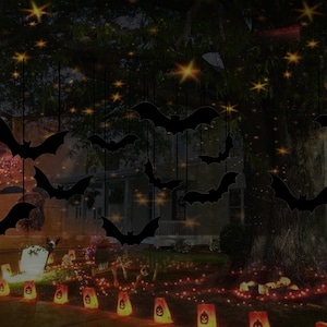 May include: A dark silhouette of bats hanging from a tree branch with twinkling lights in the background. The bats are black and the lights are yellow. There are also some orange lights on the ground in front of the tree.