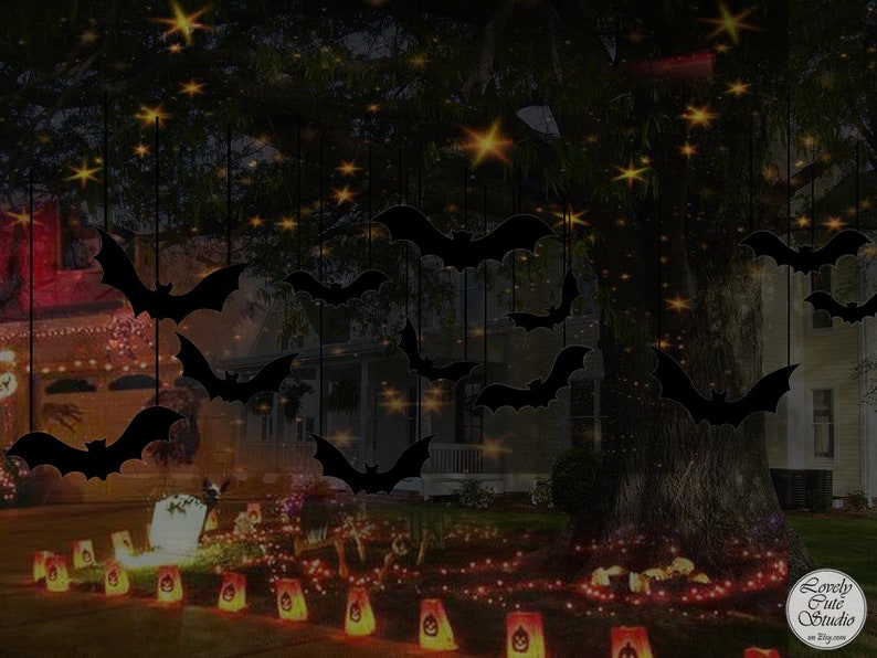 May include: A dark silhouette of bats hanging from a tree branch with twinkling lights in the background. The bats are black and the lights are yellow. There are also some orange lights on the ground in front of the tree.