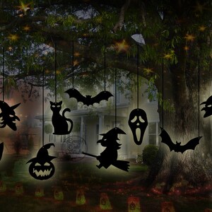 May include: Black silhouette cutouts of Halloween characters hanging from a tree branch. The characters include a witch, a cat, a bat, a ghost, a pumpkin, and a skull. The cutouts are illuminated by string lights.