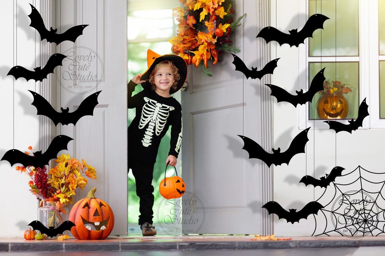 May include: A child dressed as a skeleton in a black costume and a witch hat holds a pumpkin bucket. The child is standing in a doorway decorated with black bats and a spiderweb. There are pumpkins and fall foliage on the porch.
