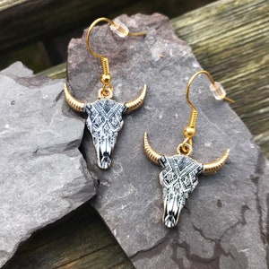 May include: A pair of gold dangle earrings with a black and white patterned bull skull design.