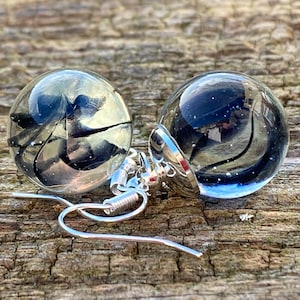May include: A pair of silver dangle earrings with clear glass orbs containing black feathers. The orbs are about 1 inch in diameter.