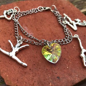 May include: A silver charm bracelet with multiple charms, including a heart-shaped crystal, a gymnast doing a handstand, and a gymnast doing a split.