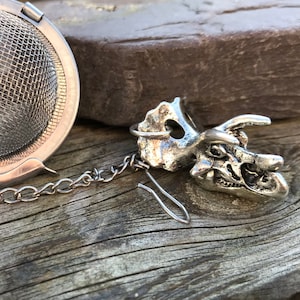 May include: Silver tea infuser shaped like a dinosaur skull with a chain attached to a round mesh strainer.