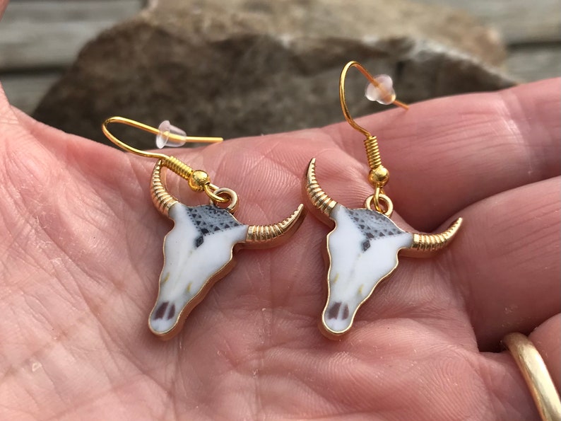 K&ouml;nnte beinhalten: Ein Paar goldfarbene Ohrringe mit einem wei&szlig;en und schwarzen Stierkopfdesign.